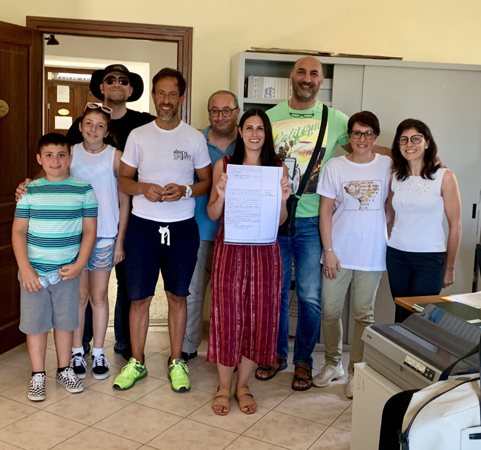 Nine people pose and smile in an office. Woman in center (Michelle) holds up a copy of an old ledger sheet.