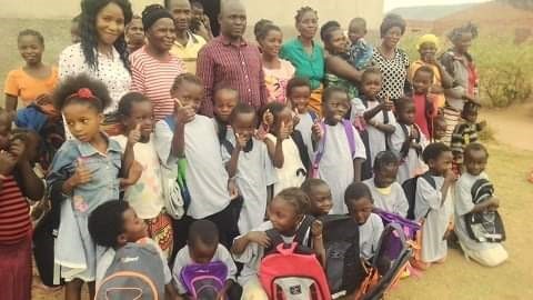 A large group of childrens smiling and giving a thumbs up. Behind them is a line of adults.